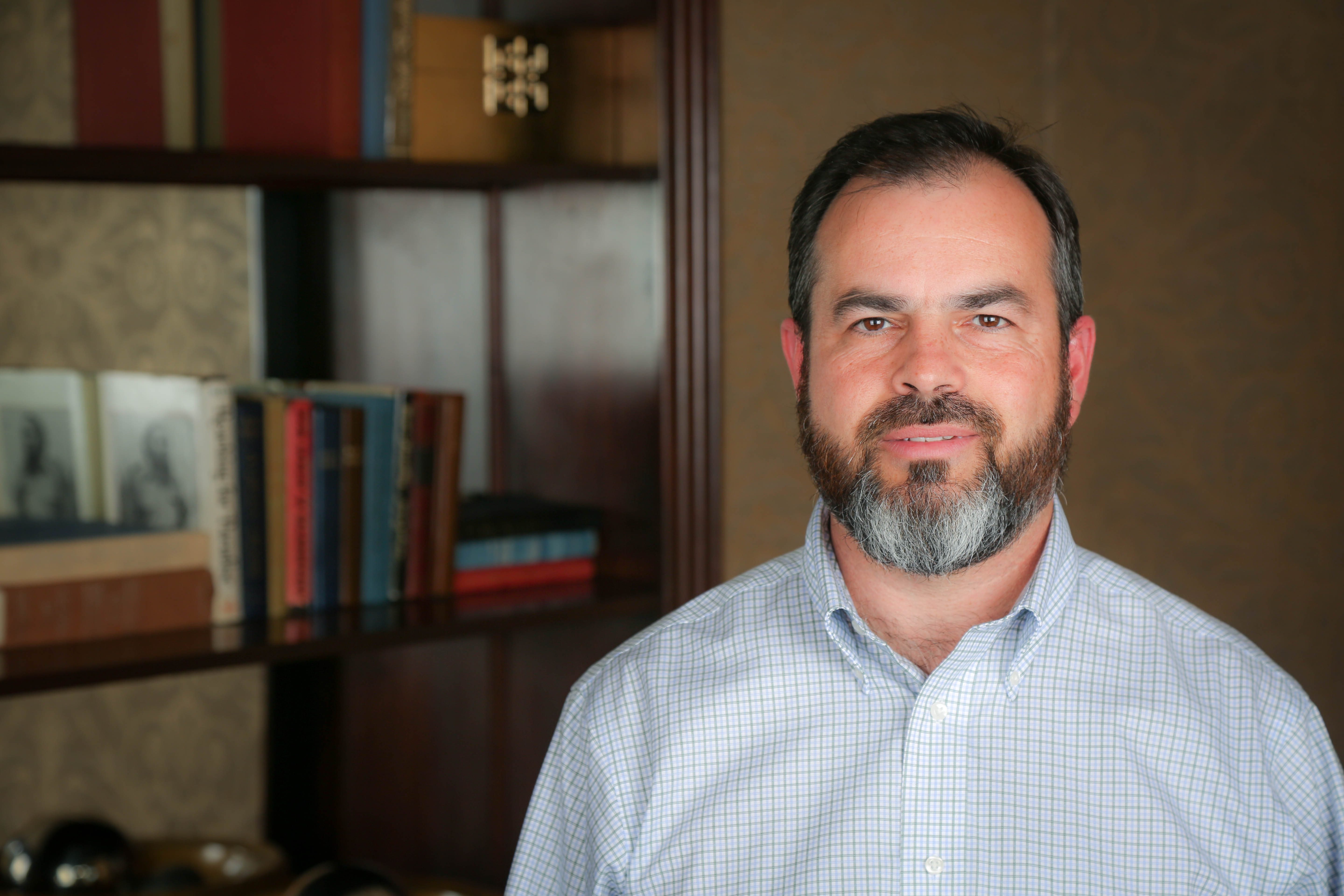 White male in button up shirt, standing in front of a bookcase